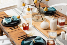 a simple fall tablescape with dark plates, blue napkins, a branch and pear centerpiece and white vases with wheat