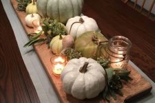 a simple farmhouse centerpiece of a wooden board with pumpkins, gourds, greenery, candles is lovely
