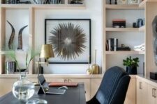 a stylish home office with a black desk and a chair, light-stained cabinets and shelves, gilded touches and artwork