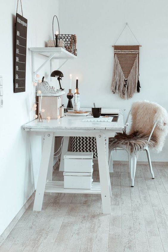 a white boho home office with a large desk, a metal chair with a pink fur cover, candles, lights and a macrame hanging