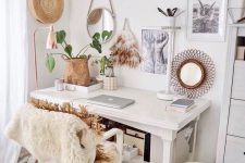 a white boho home office with a vintage desk, some chairs, faux fur and rattan, a basket, a gallery wall and some plants