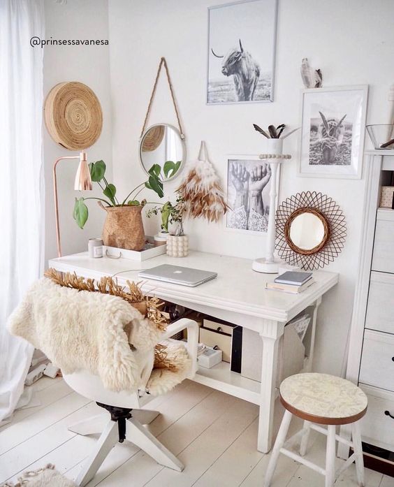 a white boho home office with a vintage desk, some chairs, faux fur and rattan, a basket, a gallery wall and some plants
