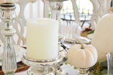 a white fall centerpiece of white pillar candles and white pumpkins in mercury glass stands