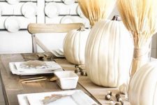 a white fall tablescape with white pumpkins, wheat bundles, acorns, white square plates and gold cutlery