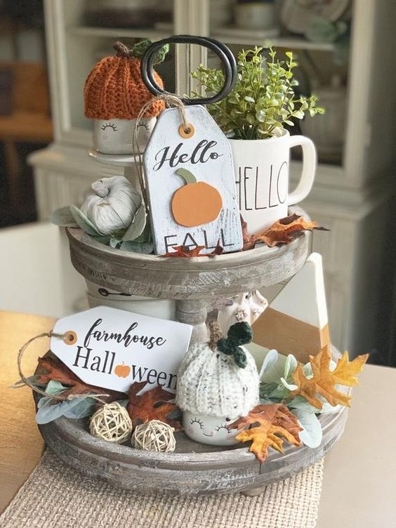 a whitewashed wooden stand with faux pumpkins, fall leaves, greenery in a mug, tags, knit pumpkin caps
