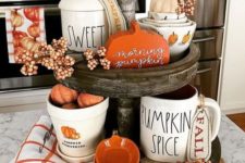a wooden stand with white and orange porcelain, berries, fake pumpkins and plaid napkins for the fall