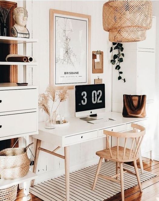 An airy boho home office with a sleek desk, a wooden chair, a rattan lamp and an open closed storage unit, pampas grass for decor