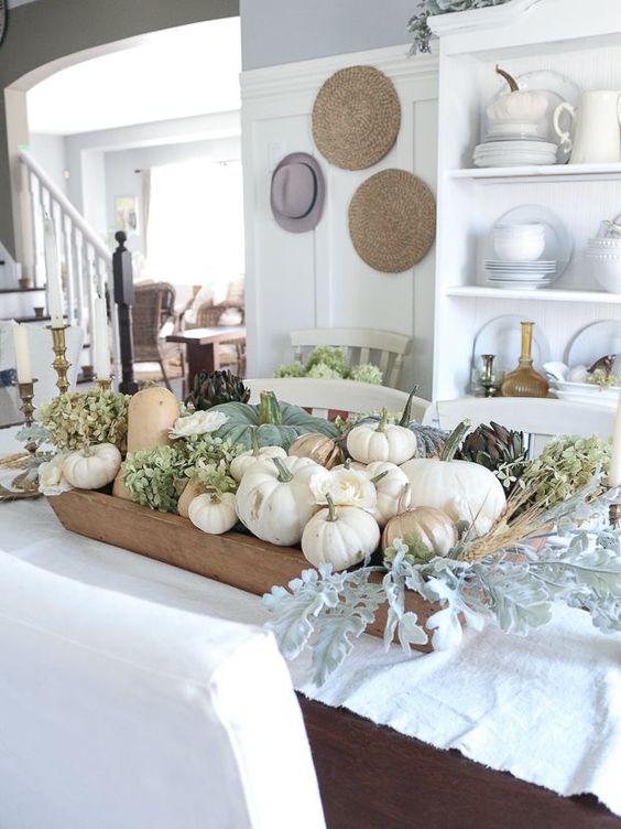 An all natural fall centerpiece of a dough bowl, neutral pumpkins, green hydrangeas and pale greenery and wheat