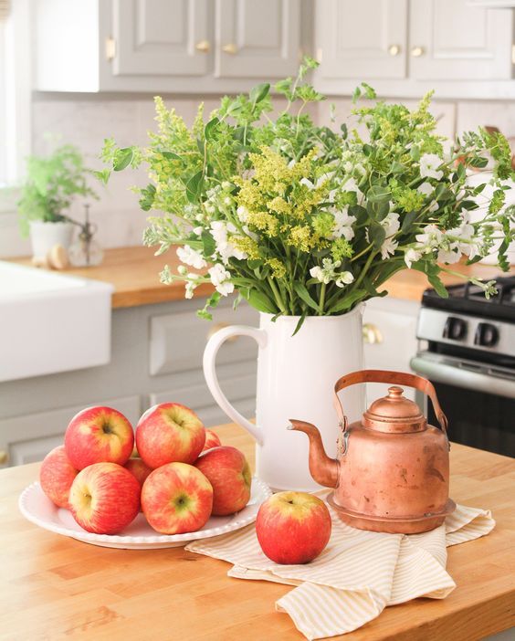 an early fall decoration - a jug with greenery and white blooms, fresh apples and a copper kettle