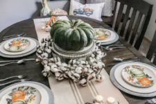 printed plates, a striped runner, candles, neutral pumpkins and cotton and a large heirloom one as a centerpiece