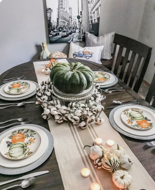 printed plates, a striped runner, candles, neutral pumpkins and cotton and a large heirloom one as a centerpiece
