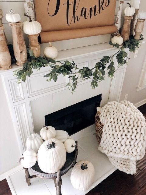 white fall fireplace styling with white pumpkins on wooden stands, white pumpkins on a vintage stand and a white chunky knit blanket