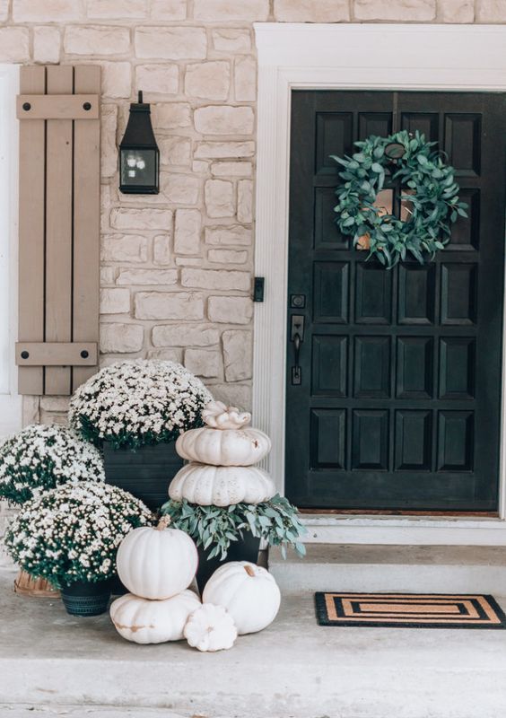 white outdoor fall decor with white potted flowers and white stacked pumpkins and greenery is very chic