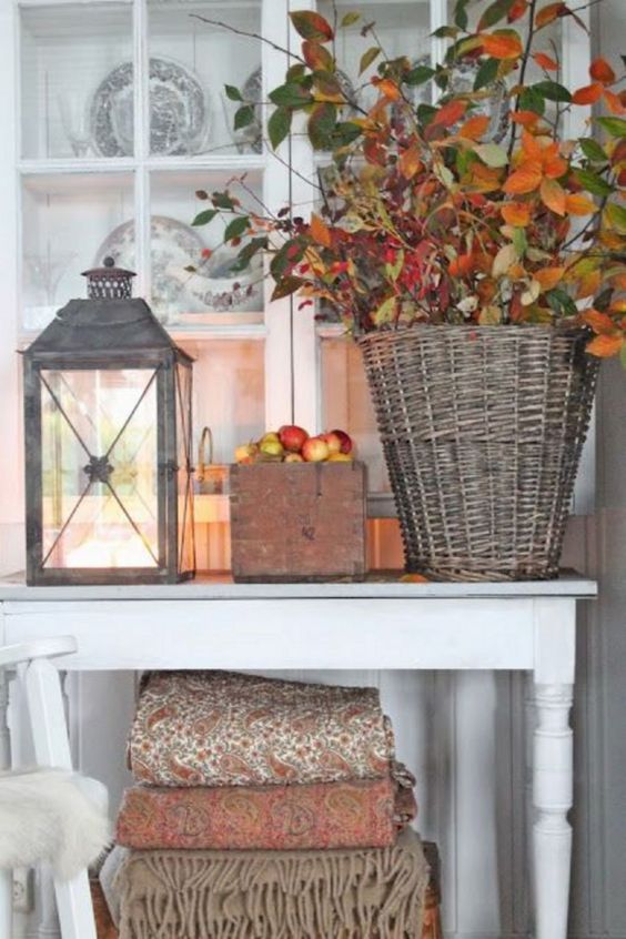 a basket with branches with berries and leaves, apples in a box and a candle lantern for a cozy touch