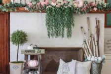 a bright fall mantel with cascadign greenery, pastel pumpkins, greenery, branches in a bucket and a wooden basket