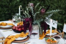 a bright fall tablescape with mustard napkins, greenery and burgundy blooms and candles