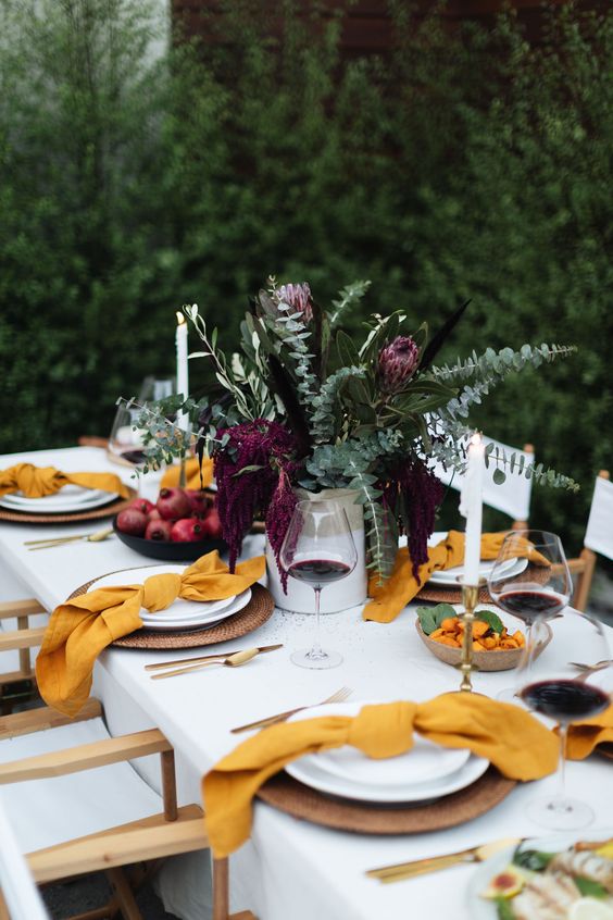 a bright fall tablescape with mustard napkins, greenery and burgundy blooms and candles