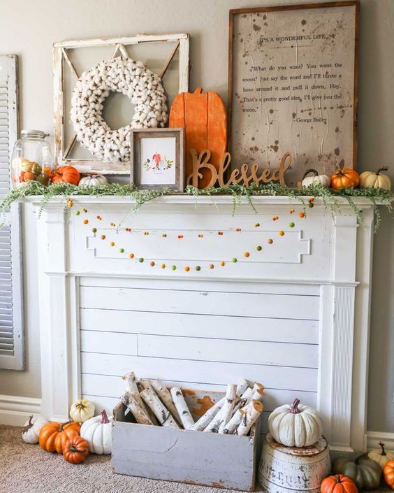 a bright rustic flal mantel with colorful pompom garlands, a crate with birch branches, lots of pumpkins, signs and a cotton wreath