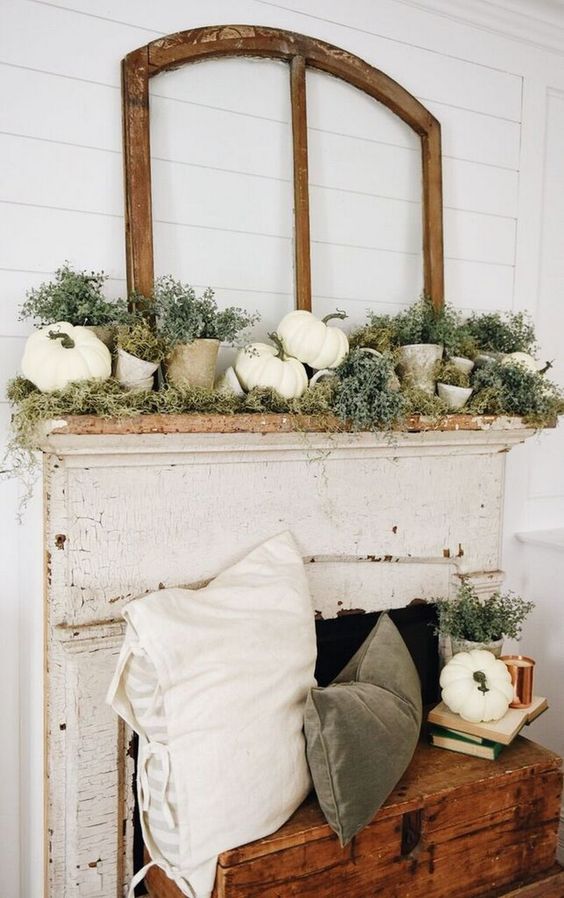 a chic rustic fall mantel with faux pumpkins, moss, greenery in terra cotta pots and with matching velvet pillows in the fireplace