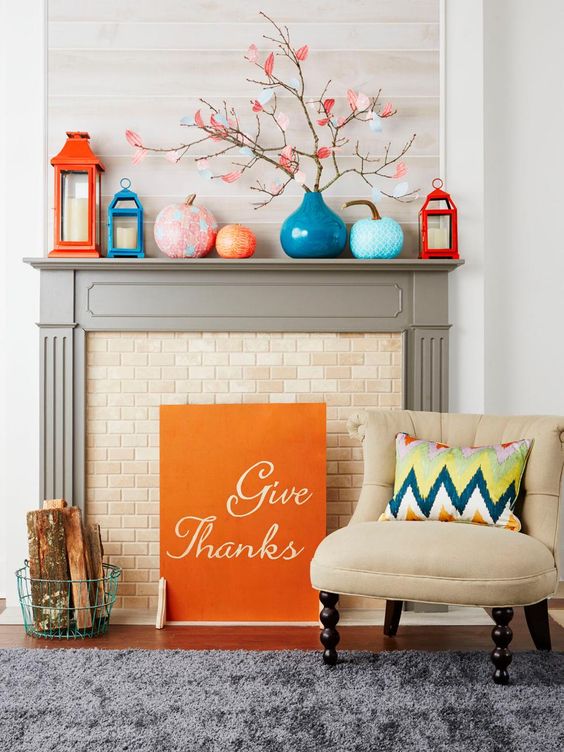 a cool colorful mantel with orange and blue candle lanterns, colorful pumpkins and branches with paper leaves