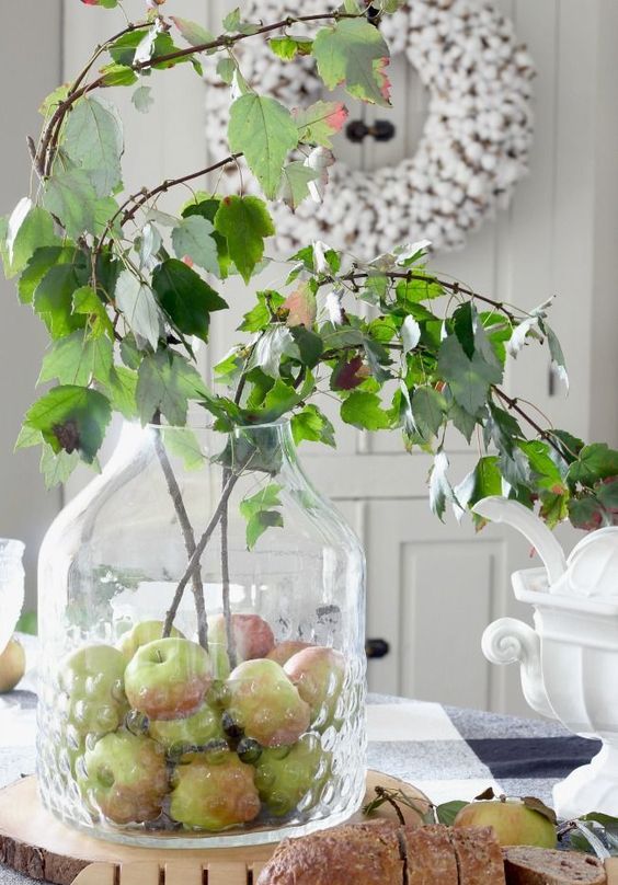 a creative fall centerpiece of a large jar with apples and some greenery branches