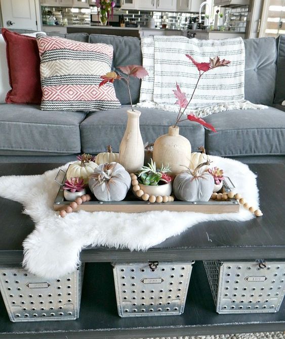 a fall coffee table styled with a wooden tray with wooden beads, natural and fabric pumpkins and red fall leaves in vases