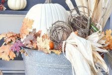 a fall decoration of a metal bucket with corn husks, leaves, pumpkins and vine balls