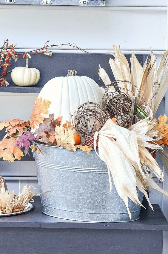 a fall decoration of a metal bucket with corn husks, leaves, pumpkins and vine balls