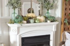 a fall mantel decorated with pinecones, faux pumpkins, pale greenery in tall bottles