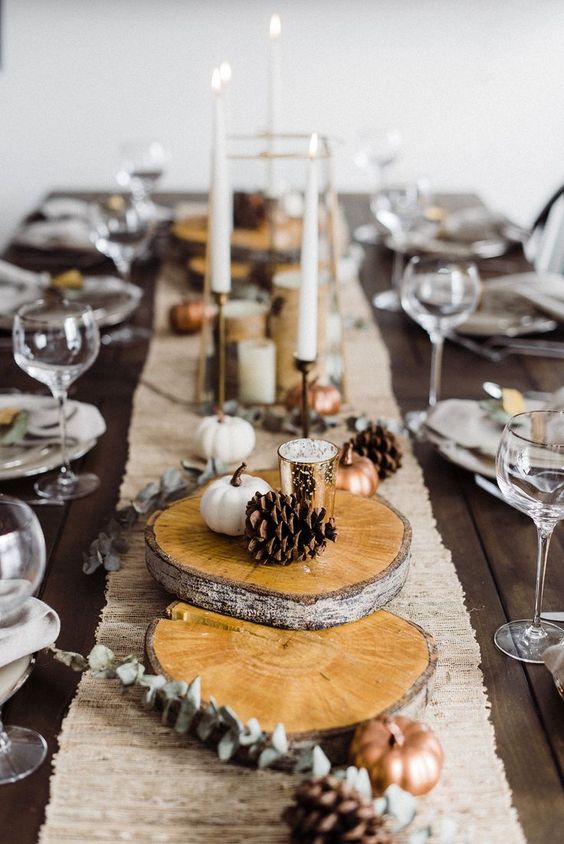 a fall tablescape with wood slices, pinecones, little faux pumpkins, a burlap runner for a natural feel