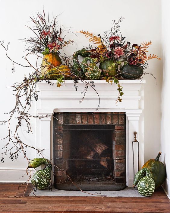 a lush harvest mantel decorated with greenery, long branches and pumpkins and gourds on the mantel