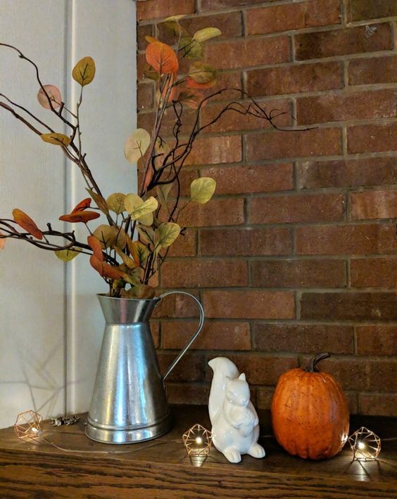 a metal jug with branches and fake fall leaves plus a pumpkin are simple fall decorations to go for