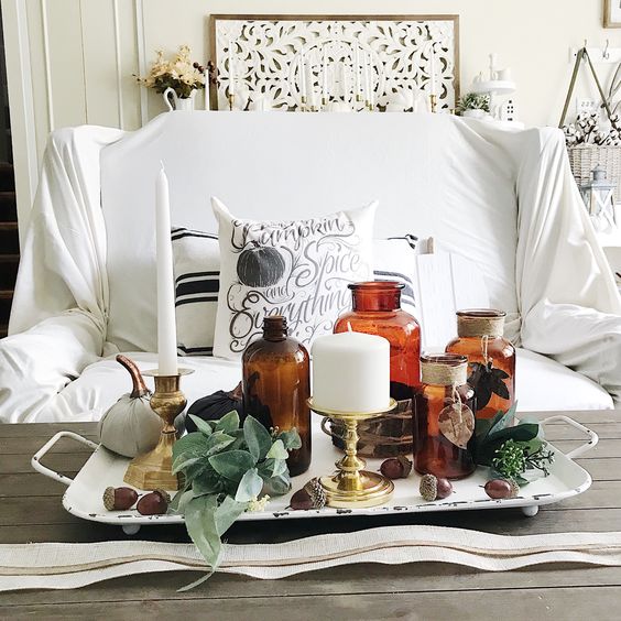 a metal tray with greenery, acorns, apothecary bottles, white candles and fabric pumpkins is a whimsy and cool decoration