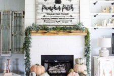 a modern farmhouse mantel with stacks of heirloom pumpkins, a greenery wreath and a large rustic sign