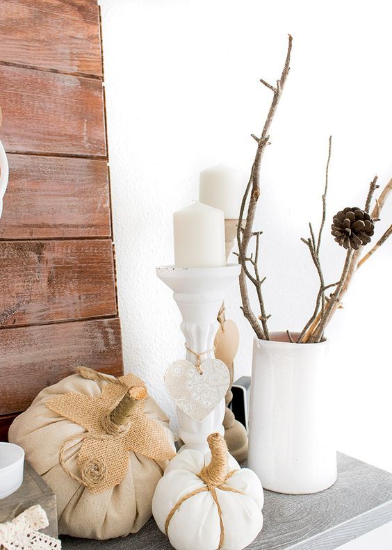 a neutral vintage-inspired mantel with branches in a white vase and some faux white pumpkins and candles