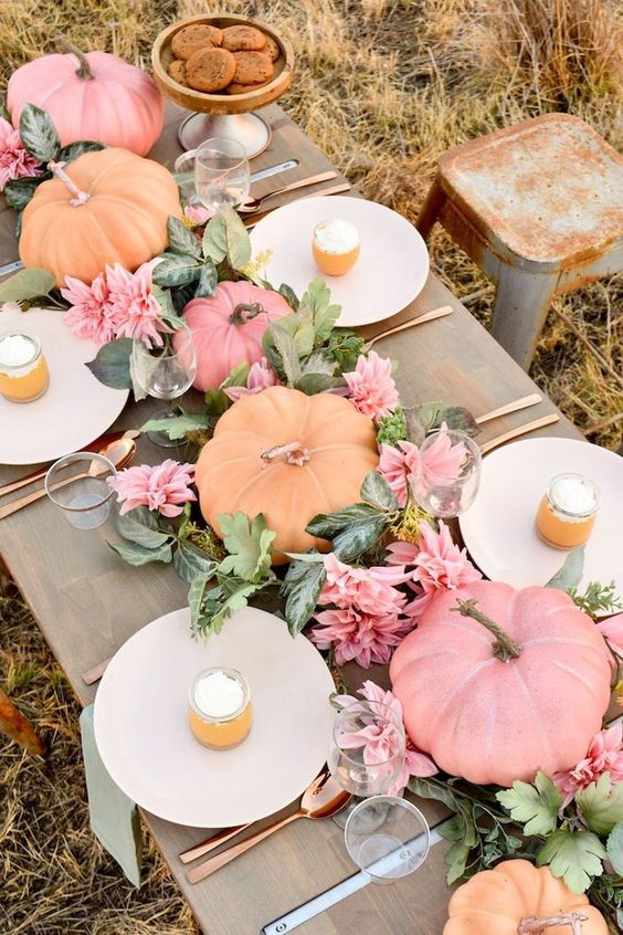 a pastel fall tablescape with pink blooms, greenery, pastel pumpkins and copper cutlery to finish off the look