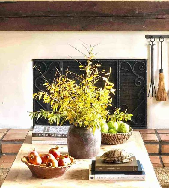 a pot with greenery branches, a wooden bowl with moss balls and a wooden bowl with pomegranates for natural decor