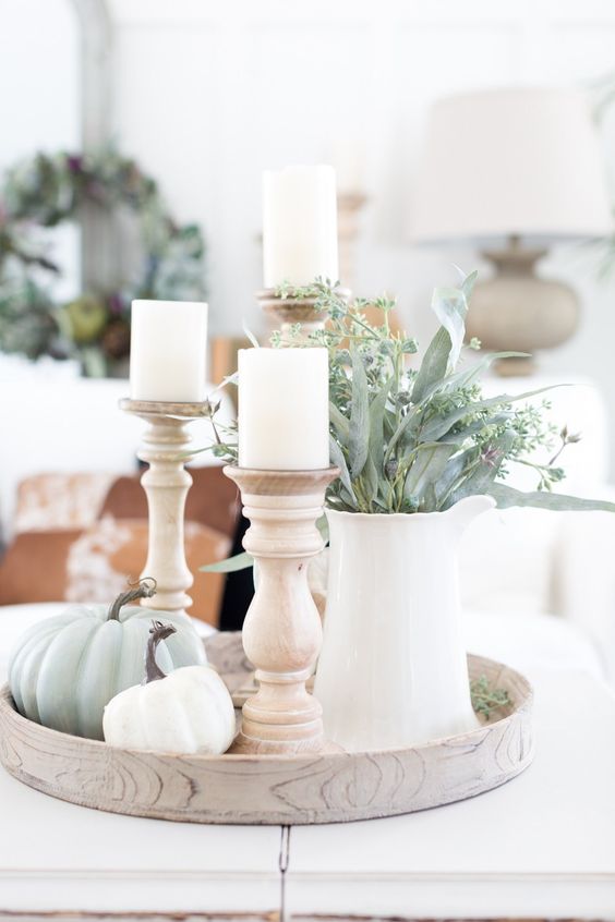 a round tray with green and white pumpkins, white candles in wooden candleholders and greenery in a white jug