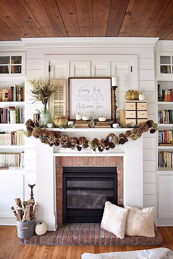 a rustic fall mantel with a pinecone and hydrangea garland, white pumpkins and faux porcelain ones, a branch arrangement in a bucket