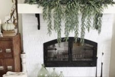 a rustic fall mantel with cascading greenery, white pumpkins with a wooden dough bowl plus green bottles