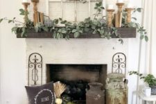 a rustic fall mantel with greenery, candles in wooden candleholders, a crate with white pumpkins, a pillow and a wood slice wreath