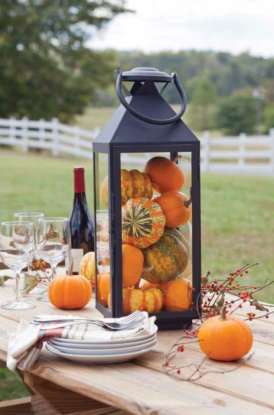 a simple and chic fall decoration of a black lantern filled with gourds and pumpkins