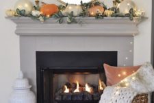 a simple contemporary fall mantel done with greenery and pumpkins of muted colors plus lights all over it