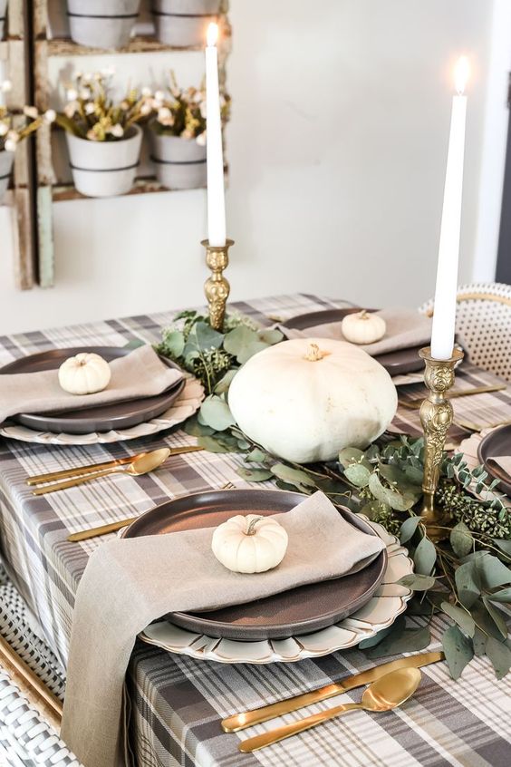A stylish low key fall party tablescape with a plaid tablecloth, eucalyptus, tall candles and gold cutlery
