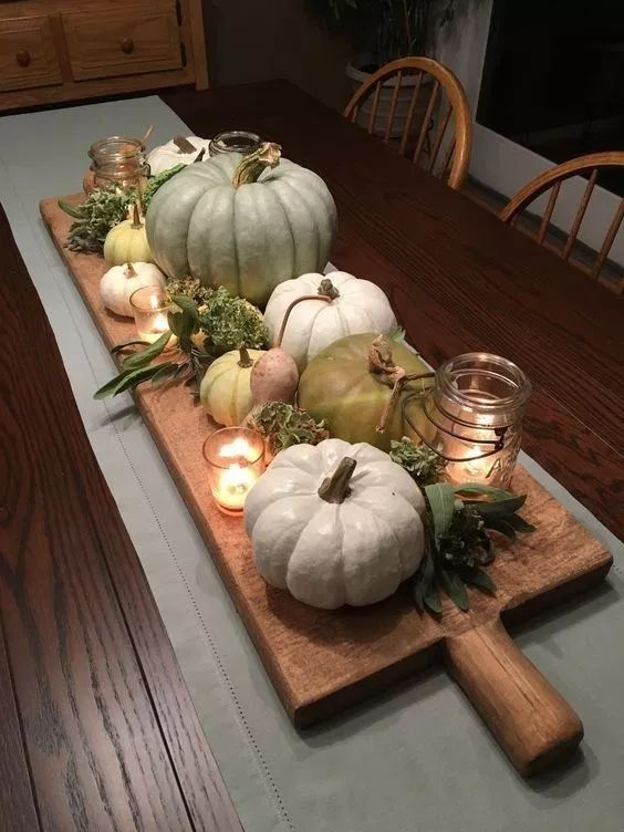 a stylish natural fall centerpiece of a cuttin board, heirloom pumpkins, greenery, candles and dried blooms