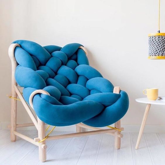 A super creative chair with a light stained wooden frame and a piece of blue upholstery all bent and wrapped to form a seat and a back