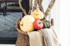 a tall basket filled with heirloom pumpkins and tree branches plus a blanket for fireplace decor
