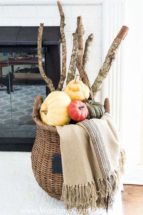 a tall basket filled with heirloom pumpkins and tree branches plus a blanket for fireplace decor