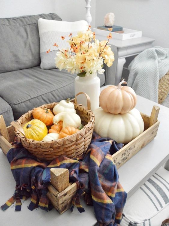 a tray with a checked napkin, a basket with faux gourds and pumpkins, a stack of pumpkins and a white vase with fall blooms