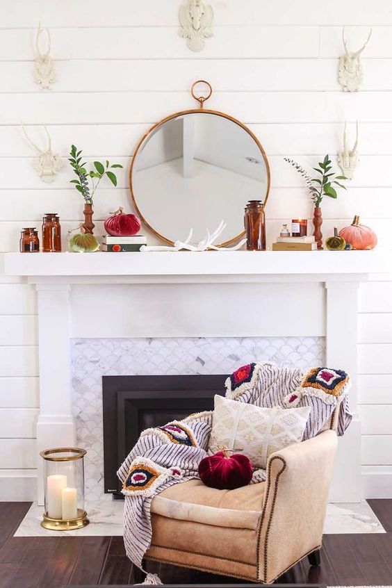 a whimsy flal mantel with brown bottles, a round mirror, greenery in vases, velvet pumpkins
